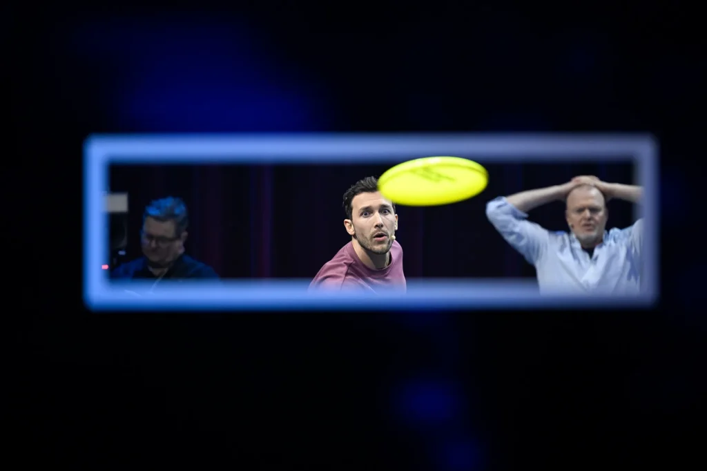 Spieler fixieren eine fliegende Scheibe in einer blau beleuchteten Spielshow