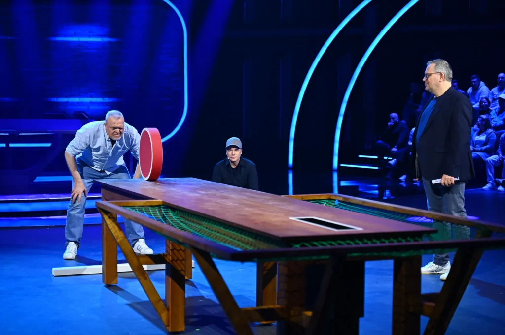 Spieler an einem großen Spieltisch in einer blau beleuchteten Showkulisse